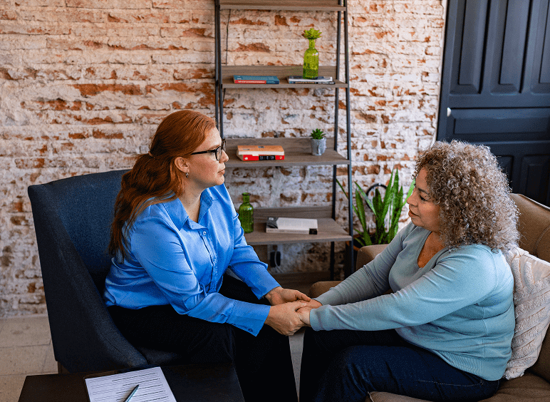 Two women sitting and holding hands, talking.